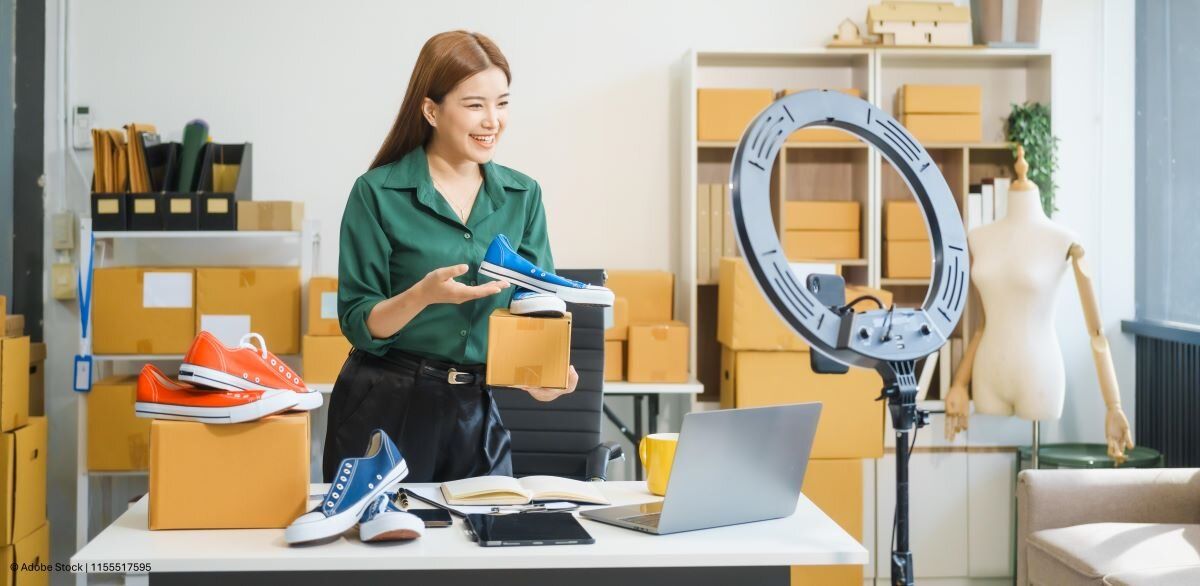 Marketing-Psychologie: Verkäuferin präsentiert für ein Video Schuhe in verschiedenen Farben vor einer Handkamera.