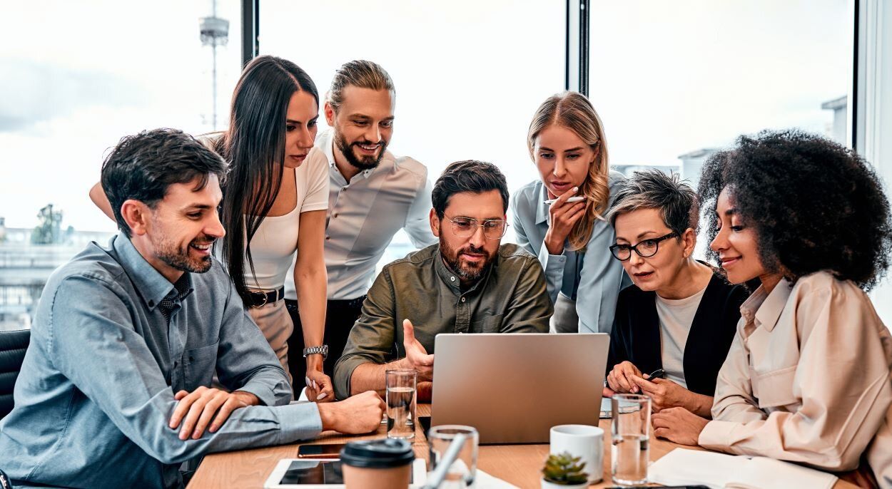 Team von sieben Personen sitzt um einen Laptop versammelt