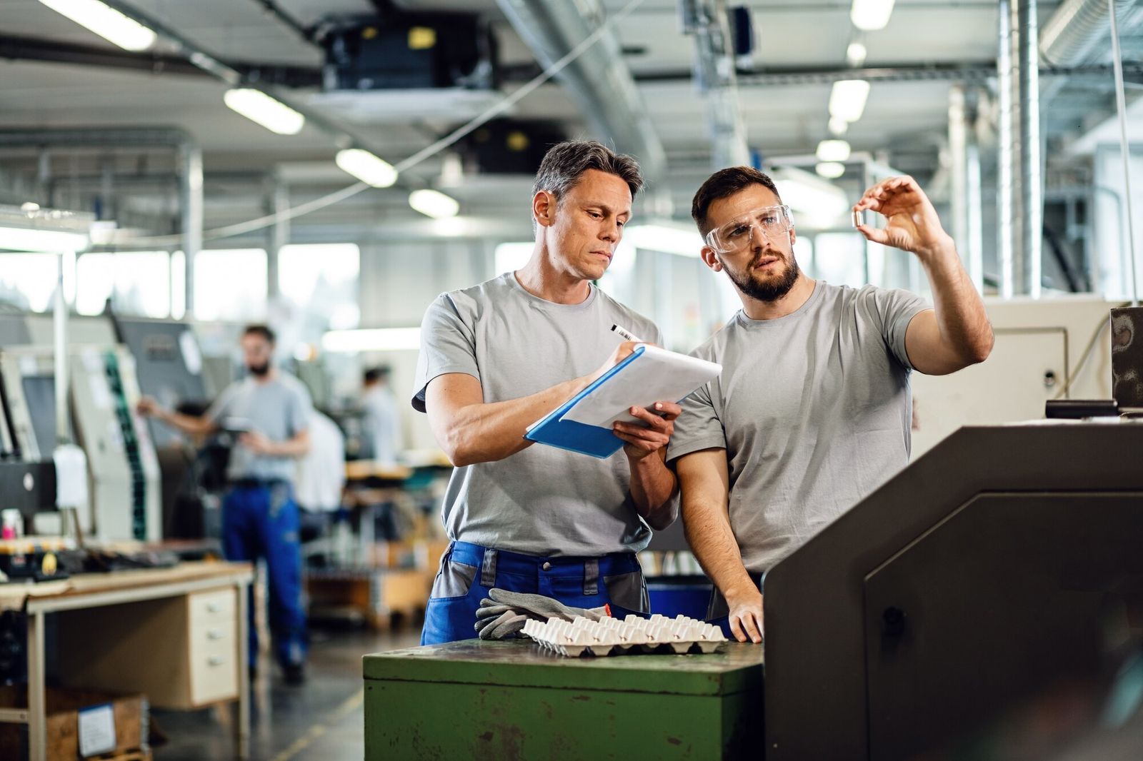 Zwei Mitarbeiter in einer Produktionshalle führen einen Qualitätscheck eines Bauteils durch