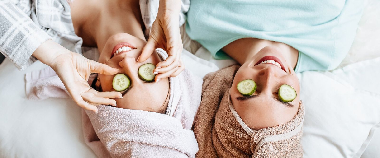 Symbolbild Gesundheitsmarketing: Blick aus der Vogelperspektive auf zwei Frauen mit Handtuch auf dem Kopf und Gurkenscheiben auf den Augen