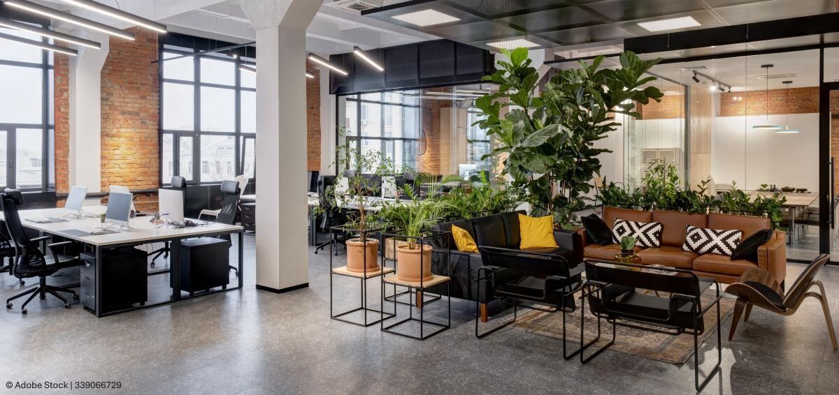 Modernes Büro mit Lounge-Ecke, Schreibtischen, Meeting-Räumen und Pflanzen in einem großen, offenen Raum.