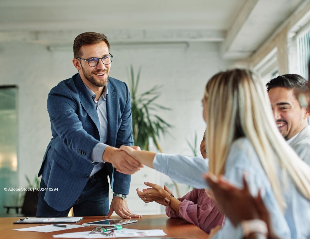 Kooperation zwischen Unternehmen: Zwei Geschäftspartner geben sich die Hand an einem Meeting-Tisch.